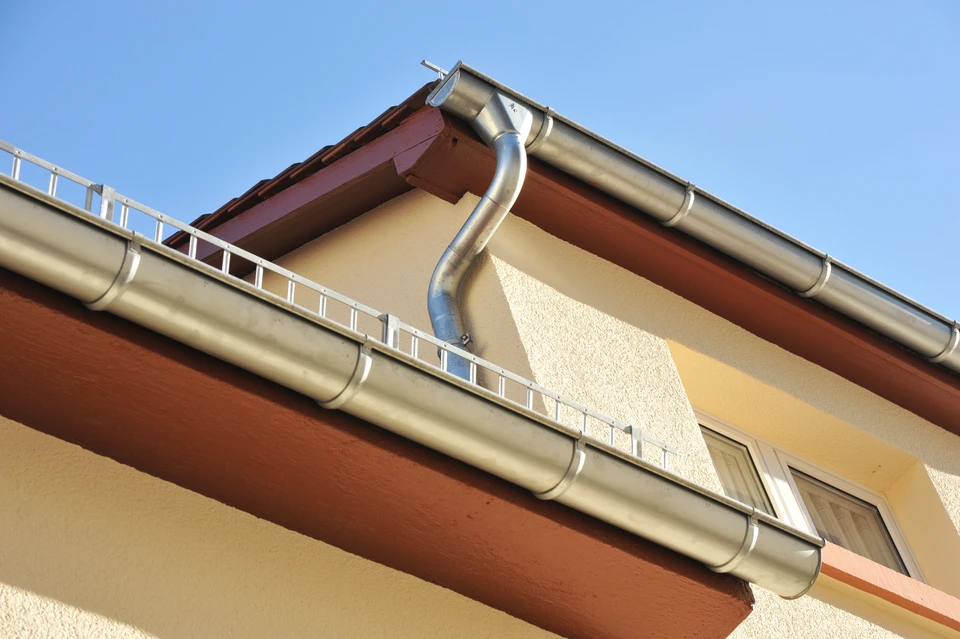 Extérieur d'un bâtiment sous ciel nuageux montrant la sous-face d'un toit avec système de gouttière métallique
