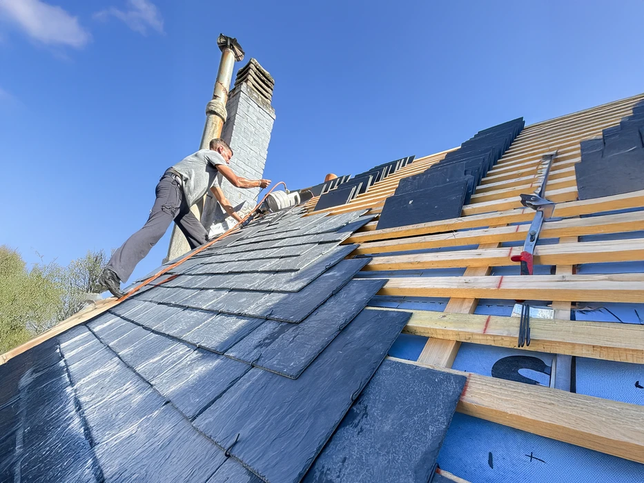 Couvreur en tenue de s&eacute;curit&eacute; travaillant sur toiture en bardeaux d'asphalte au coucher du soleil